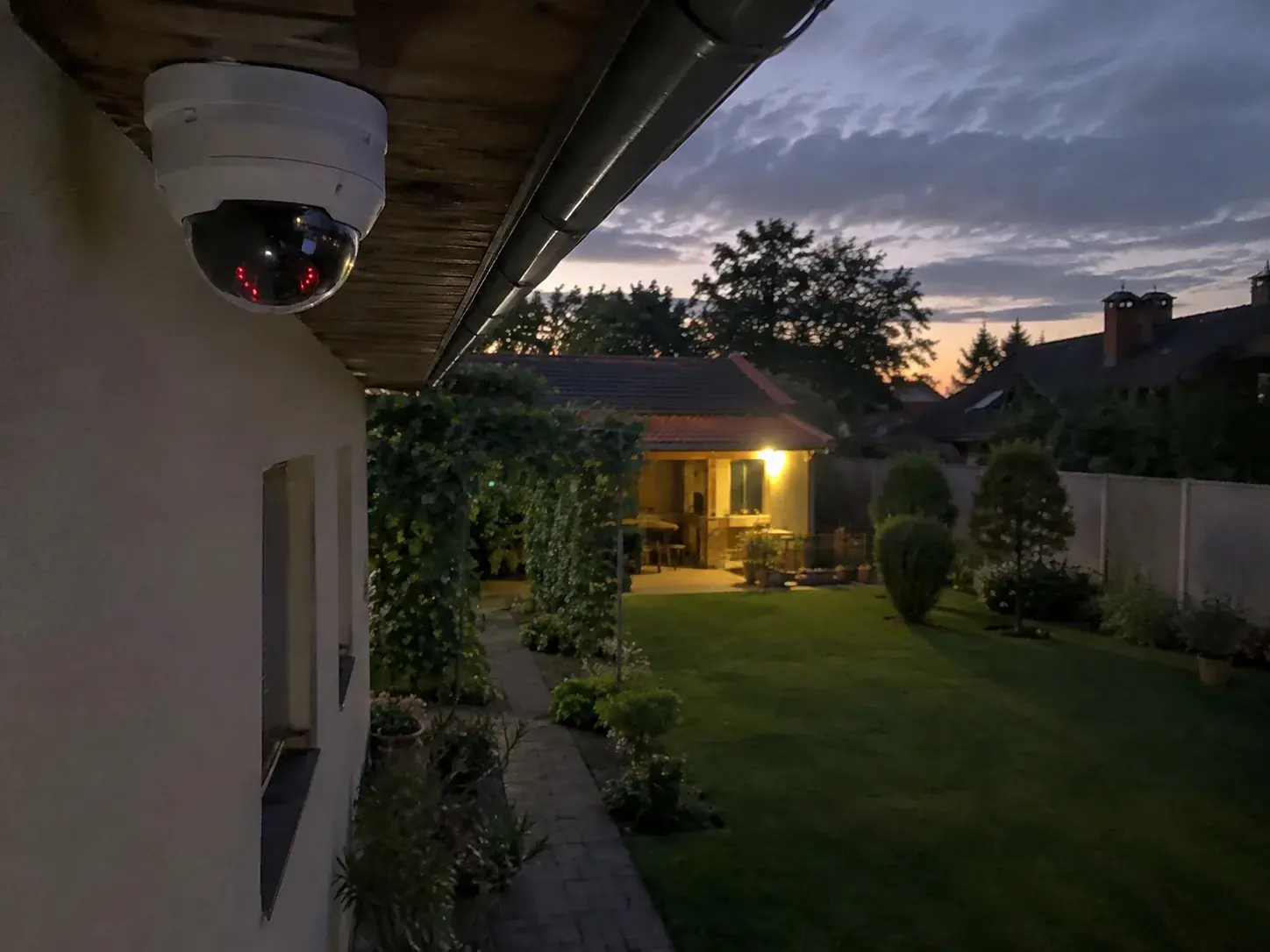 Dome kamera pod strehom sa upaljenim IR diodama nadgleda dvorište u sumrak