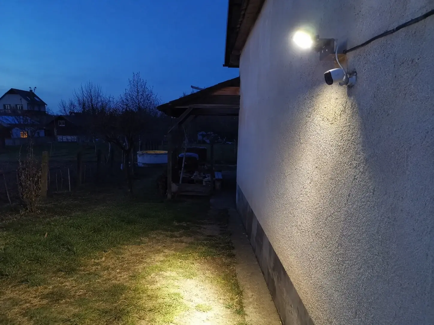Reflektor sa senzorom pokreta pored kamere obasjava dvorište u sumrak