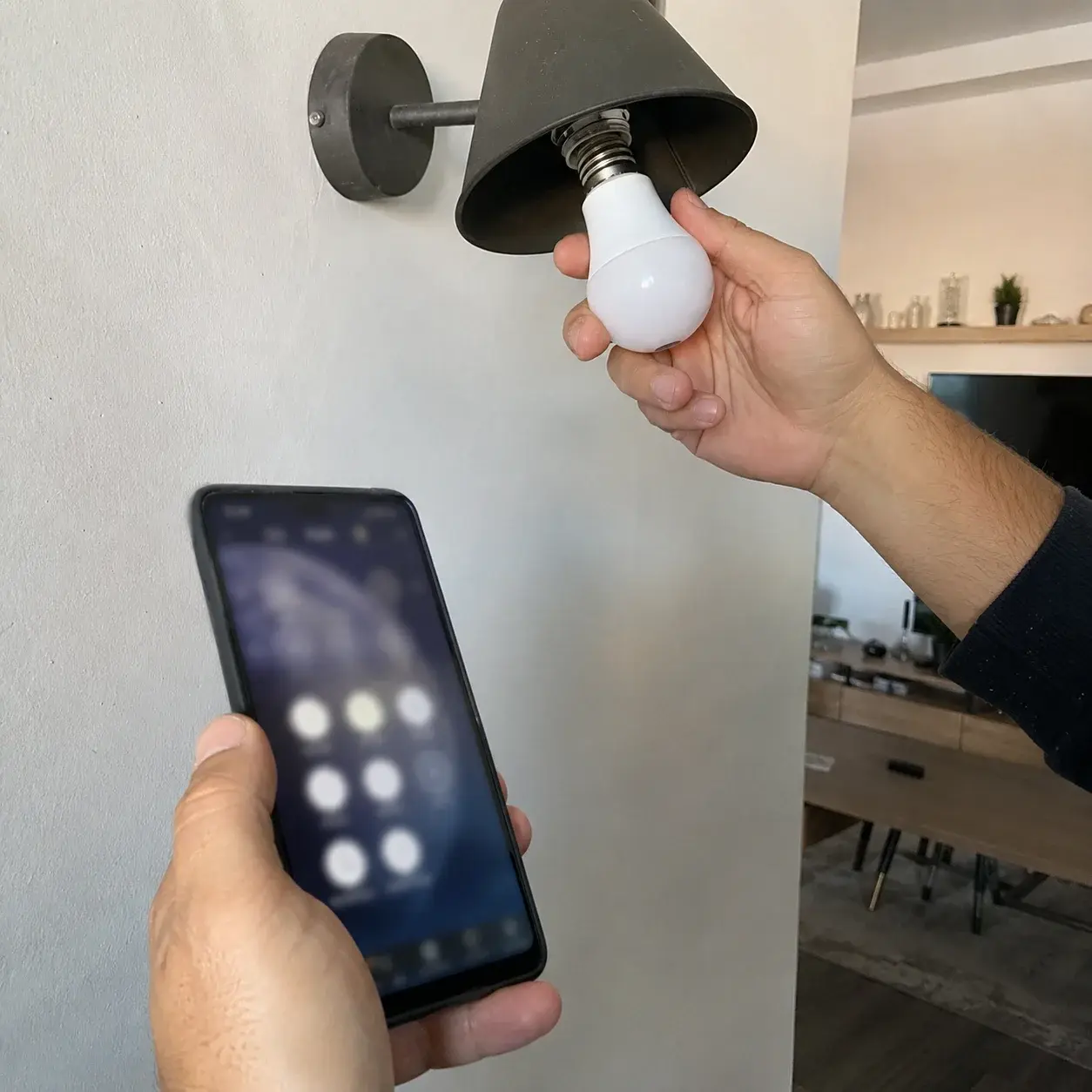 Ruka uvija pametnu LED sijalicu uz telefon sa otvorenom aplikacijom