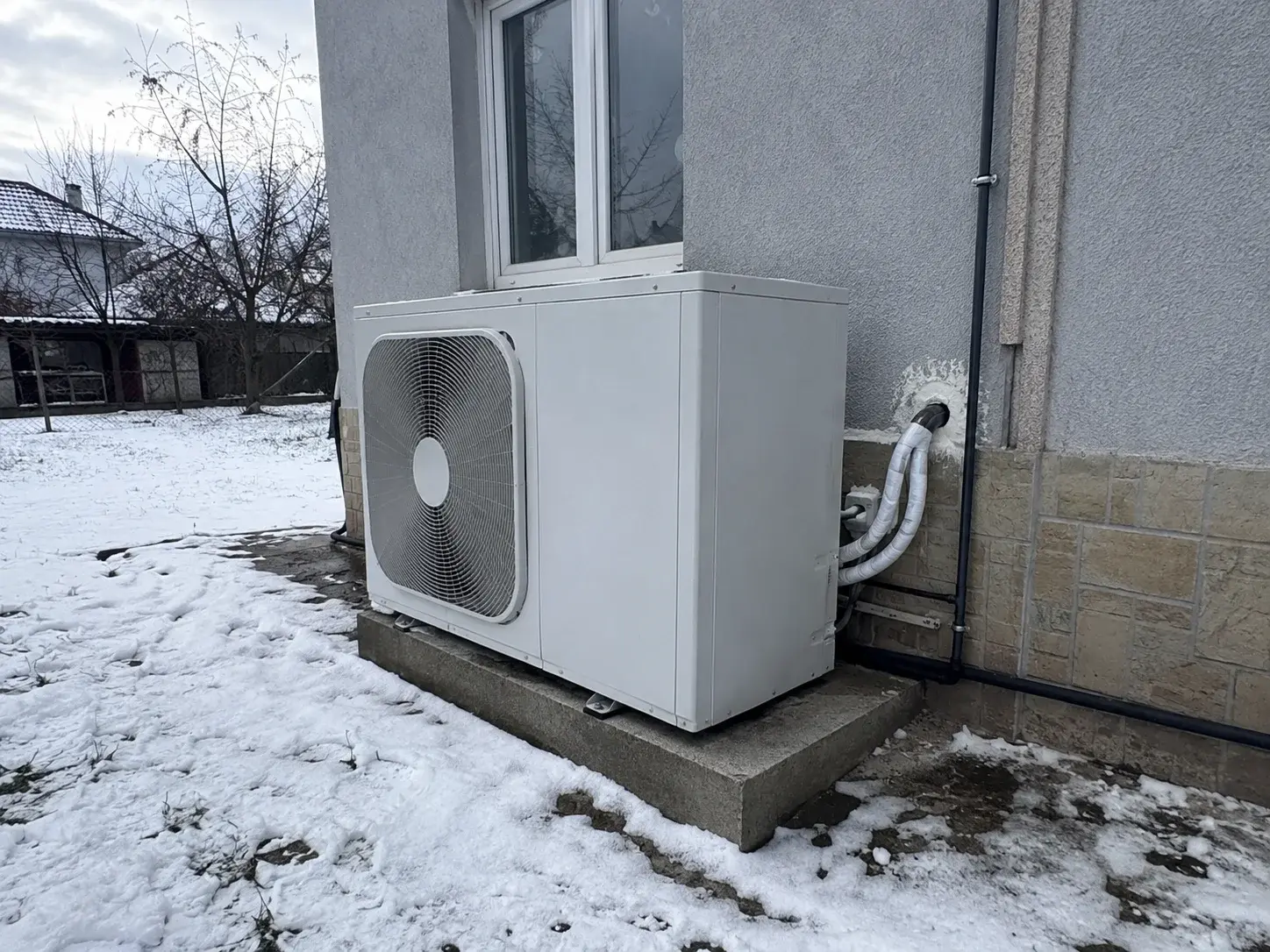 Spoljna jedinica toplotne pumpe postavljena pored kuće u zimskom periodu