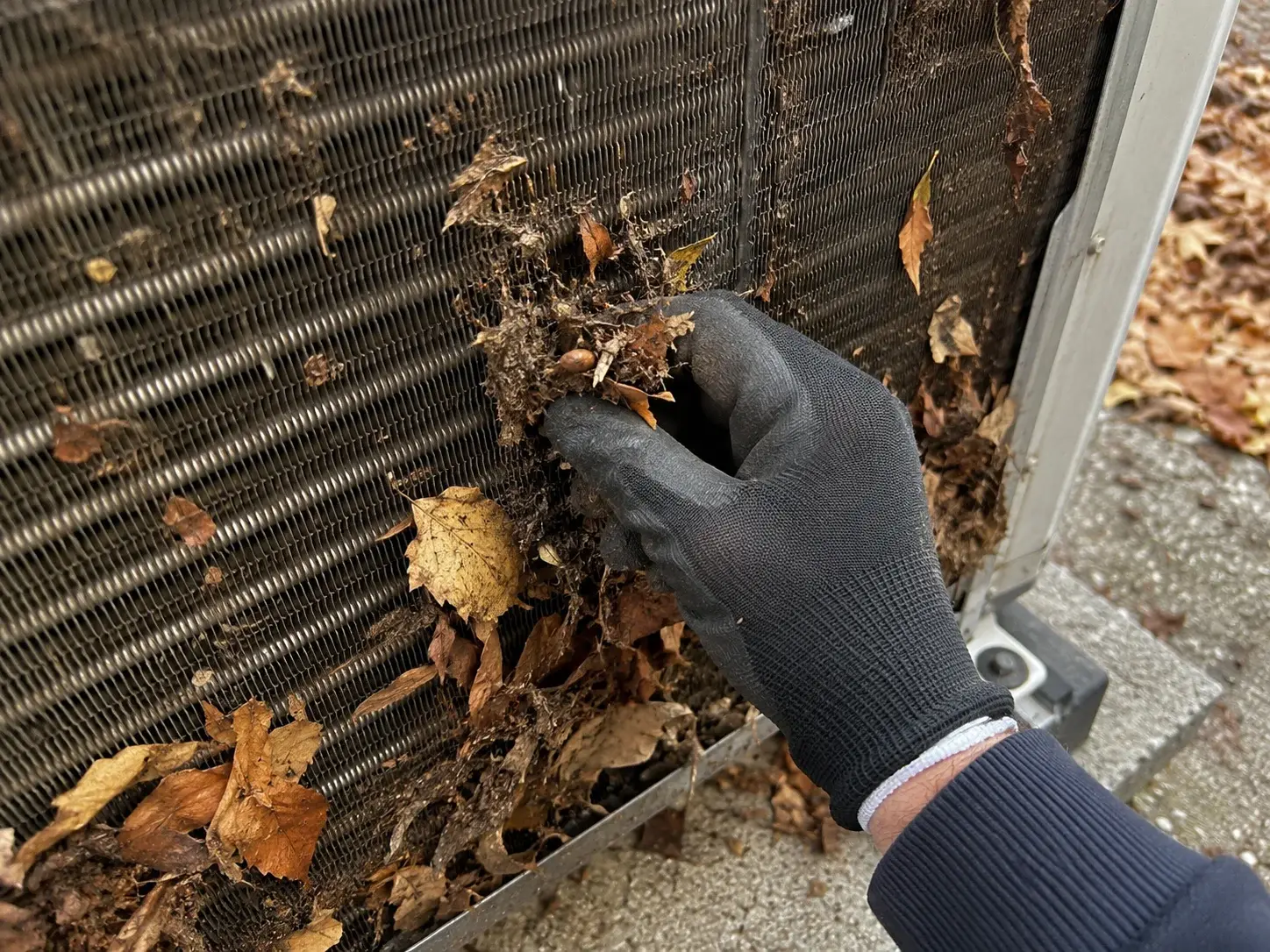 Ruka uklanja lišće i prašinu sa lamela spoljne jedinice toplotne pumpe